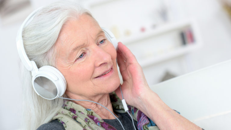 Egy idős nő fejhallgatón zenét hallgat.