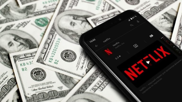 Netflix logo egy okostelefon kijelzőjén és százdolláros bankjegyek.