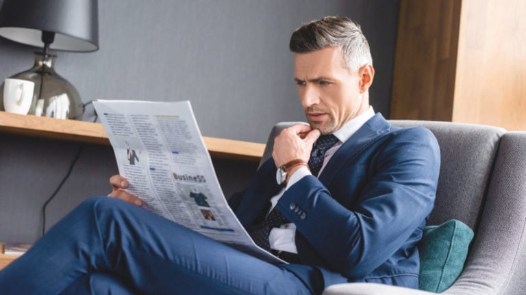 Üzletember öltönyben karosszékben ül és újságot olvas egy hotelben.