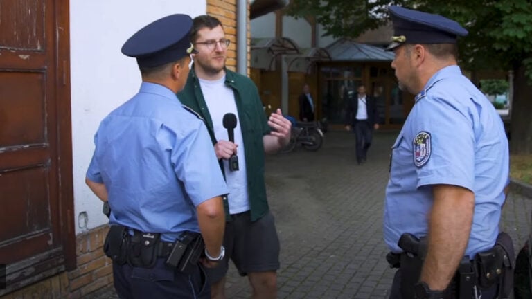 Rendőrök veszik körbe a Telex munkatársait Szijjártó Péter nyilvános fóruma előtt, hogy megakadályozzák munkavégzésében